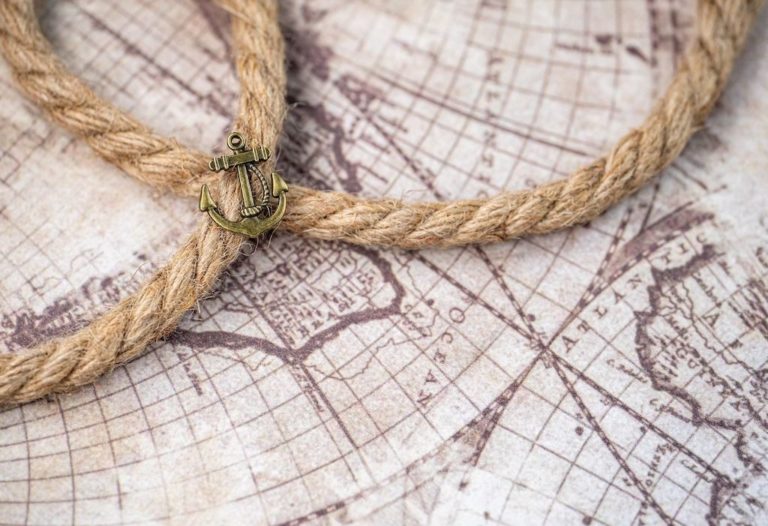 old map of the world, a piece of rope on top of the map, a metal anchor pin on top of the rope. Boating Right of Way Guide