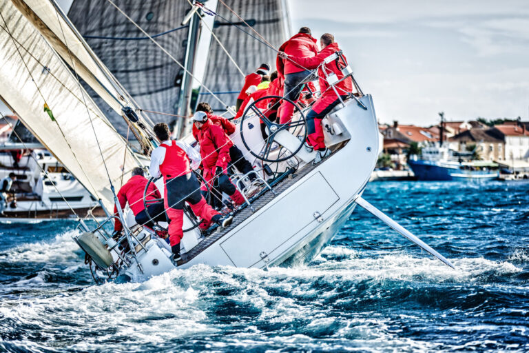 A group of sailors actively maneuvering a sailboat in rough waters. Discover the rich history of yachting, from royal vessels to modern superyachts, and embrace the ultimate luxury lifestyle. Read now!
