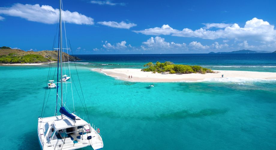 A catamaran sailing in the blue ocean near an island.