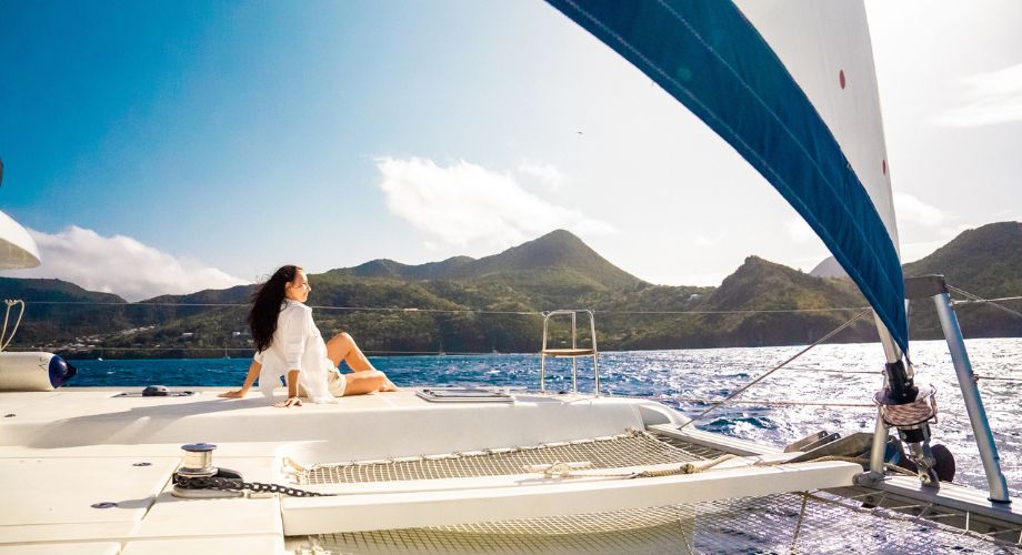 A woman sitting on a catamaran or a monohull that's sailing in the ocean. Compare catamarans vs monohulls to find the best fit for your sailing style. Learn about cost, speed, stability, and more.