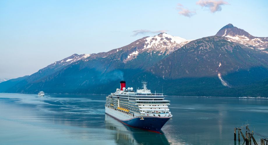 A cruise ship sailing on the ocean near a mountain. Explore pros & cons of a cruise ship vs. yacht. Compare charter cruise options, exclusive amenities, & costs for ultimate luxury sea escape.