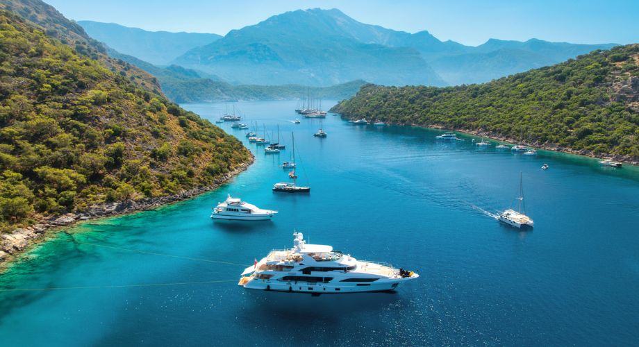 Luxury yachts sailing in the ocean between green hills. Track and organize listings with ease by using the updated YATCO BOSS, “Saved Yachts” feature—your tool for smart yacht sales management.