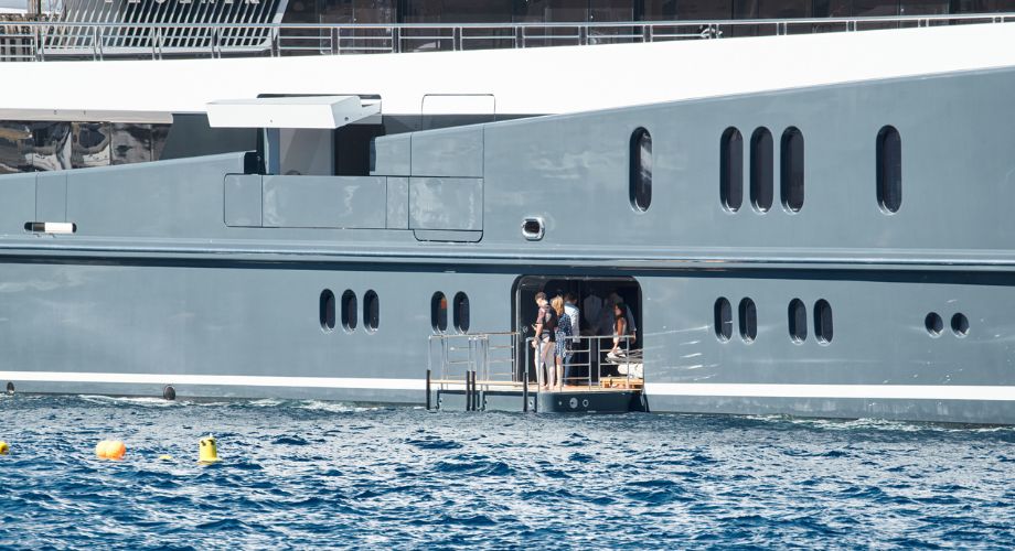 A group of people stands on a small platform extending from the side of a luxurious yacht, enjoying the view over the open sea.