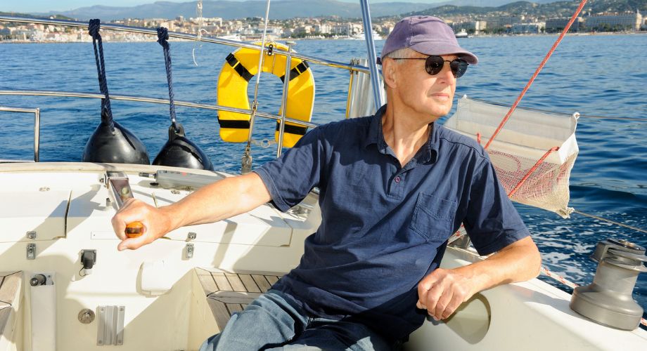 A man sitting on a luxury vessel that's sailing in the ocean and has a sailboat autopilot. Explore sailboat autopilot systems, including installation costs, and how autopilots improve your sailing experience.