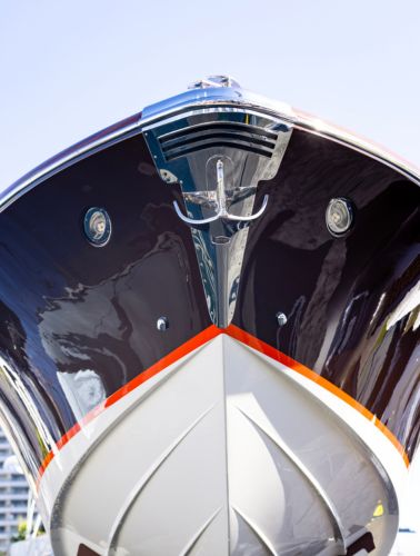 A close-up, low-angle view of the bow of a sleek, modern yacht with a glossy finish, metallic anchor, and a sharp, clean design accentuated by a red stripe.