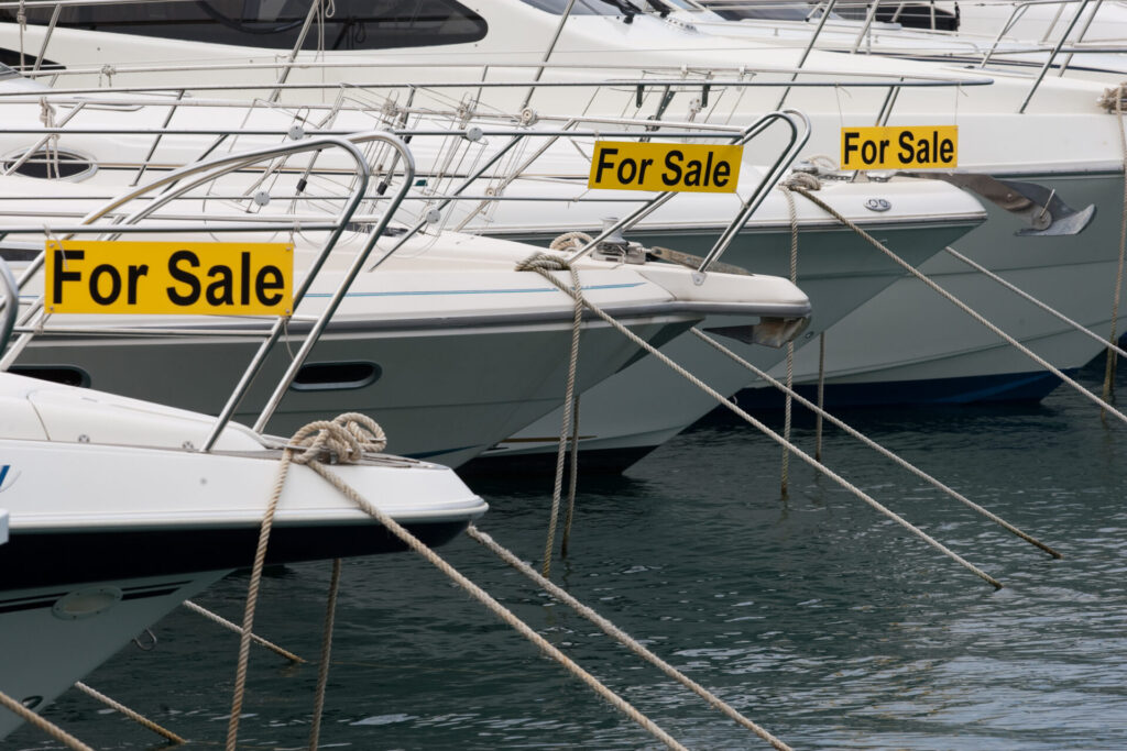 Yachts were docked in the ocean, each with a 'For Sale' sign hanging on it.