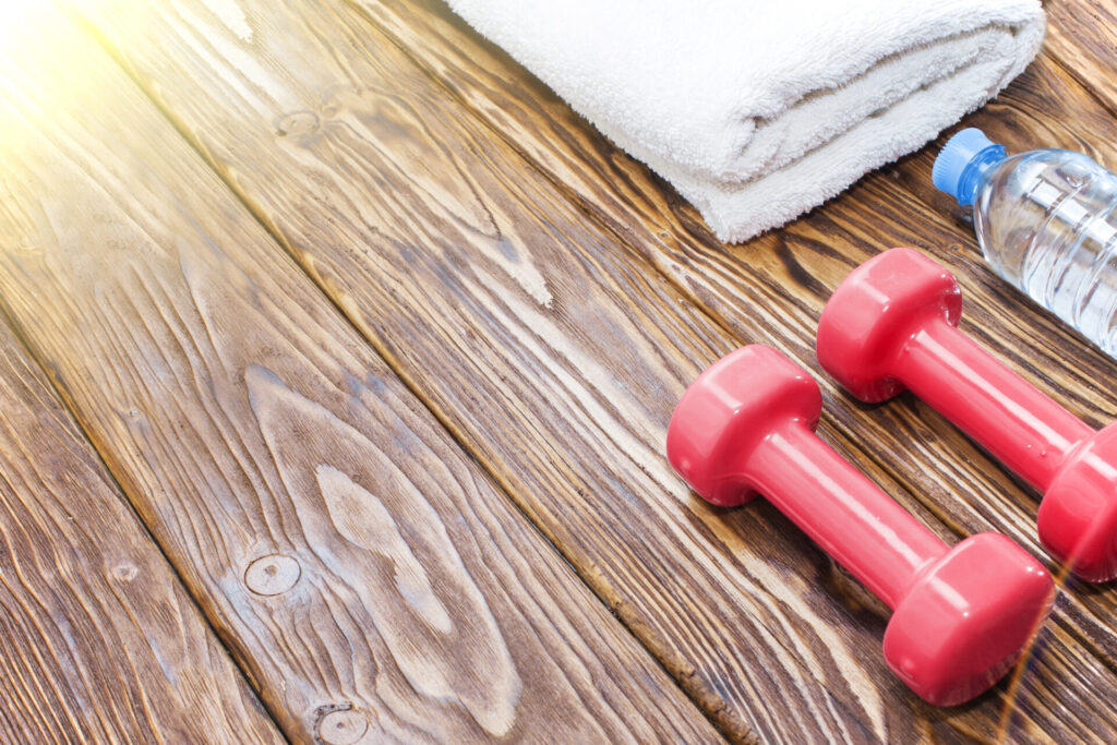 Gym dumbbells, water bottle, and towel on a wooden floor.