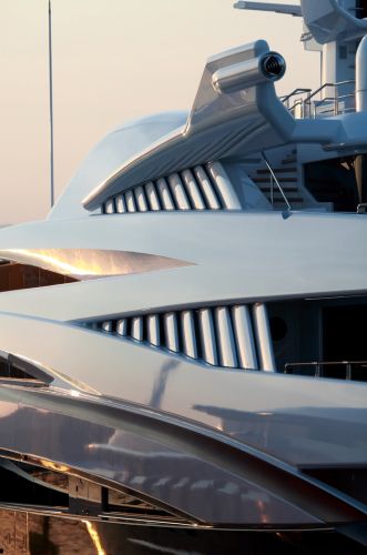 A futuristic, sleek luxury yacht with aerodynamic design elements and metallic detailing is docked at sunset.