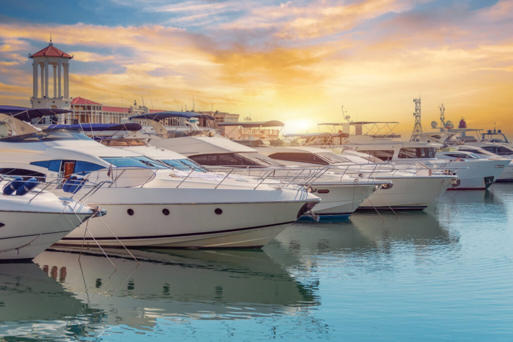 The blue water reflects orange sunset sky. Rows of sailing yachts, motor boats and fishing boats.
