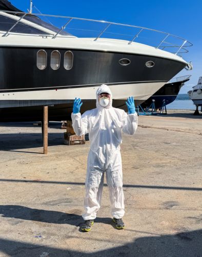 A man dressed in the yacht antifouling suit, standing in front of the yacht.