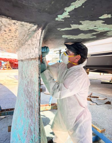 A man dressed in an antifouling suit, applying antifouling to the yacht.