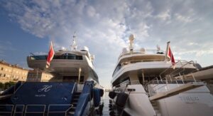 Two luxury yachts with Valletta yacht registration are docked side by side at a marina under a partly cloudy sky.