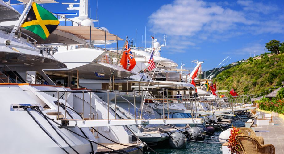 Yachts are docked in the ocean, each flying a different registered yacht flag.