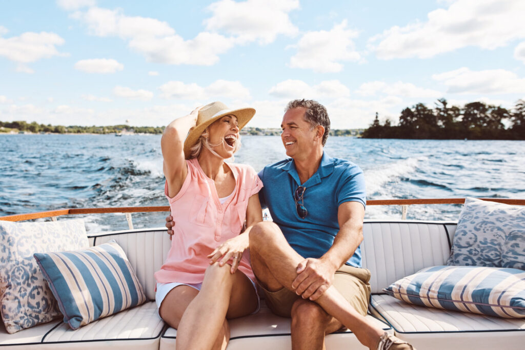 A joyful couple relaxes on a stylish yacht, laughing together as they cruise across open water under a sunny sky—capturing the carefree spirit of yachting life.