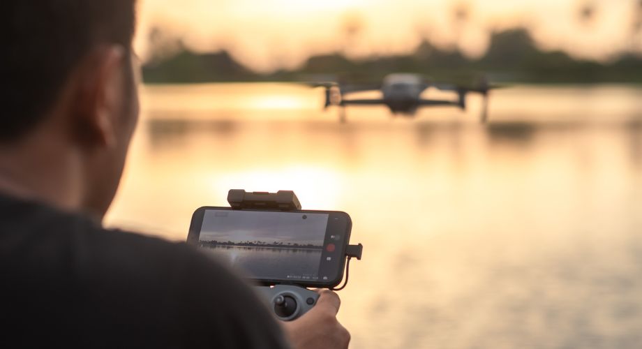 The drone pilot's hand is holding a remote control to control the drone. Explore how drone technology is transforming the yachting experience—from aerial filming and security to guest services and innovation at sea.