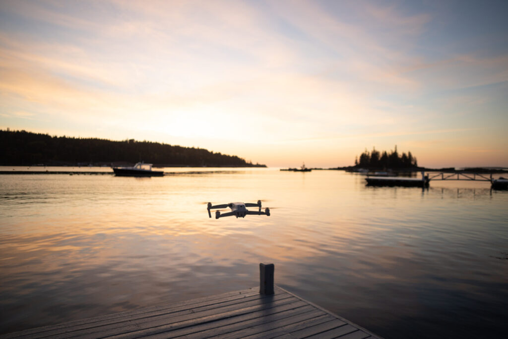 Drones on Deck | Capturing the Yachting Experience | YATCO A drone hovering off the water at sunrise on Mount Desert Island in Maine in the fall.