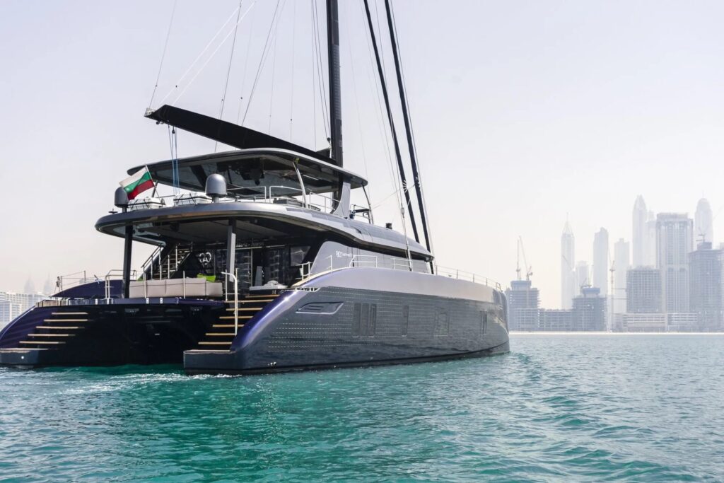 Electric Mega Yacht | Silent and Eco-Friendly Cruising | YATCO The Sunreef 80 Eco exterior showcases a luxurious electric mega yacht gliding through turquoise waters with a modern city skyline in the background.