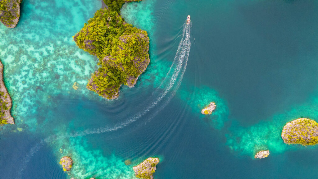 Electric Mega Yacht | Silent and Eco-Friendly Cruising | YATCO An Areal image of a boat racing through the small tropical islands of Raja Amat.