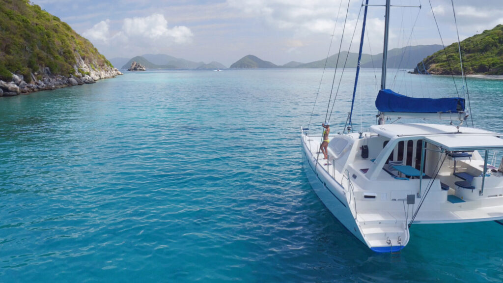 Last Minute Yacht Charter | Where to Find Deals | YATCO Woman relaxing on a beatiful Catamaran anchored in clear tropical water in the Caribbean.