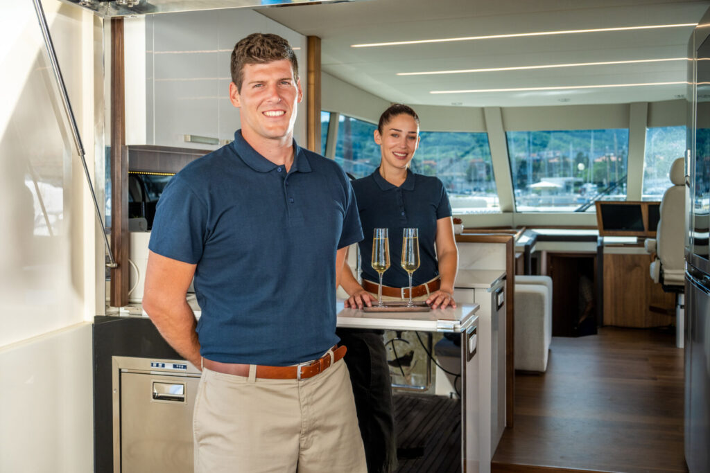 Mega Yacht Charter Business | Can You Make a Profit? | YATCO Portrait of smiling skipper and stewardess standing in luxury mega yacht charter. Is chartering a mega yacht profitable? Explore the economics, costs, and realistic returns of running a luxury yacht charter business.