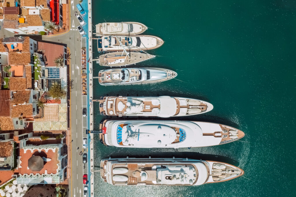Mega Yacht vs Superyacht | Differences, Sizes & Prices | YATCO Aerial top view of luxury mega yacht vs superyacht in Puerto Banus marina, Marbella, Spain.