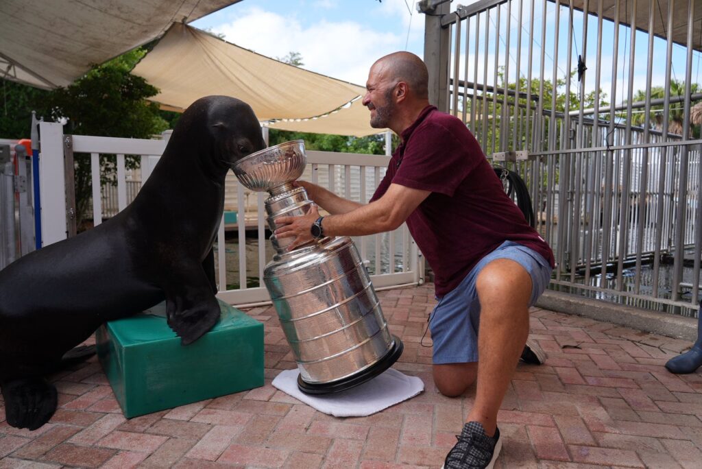 A man holding a trophy with a seal next to him. The Stanley Cup made a splash in the Florida Keys as part of the Florida Panthers’ ongoing championship celebration.