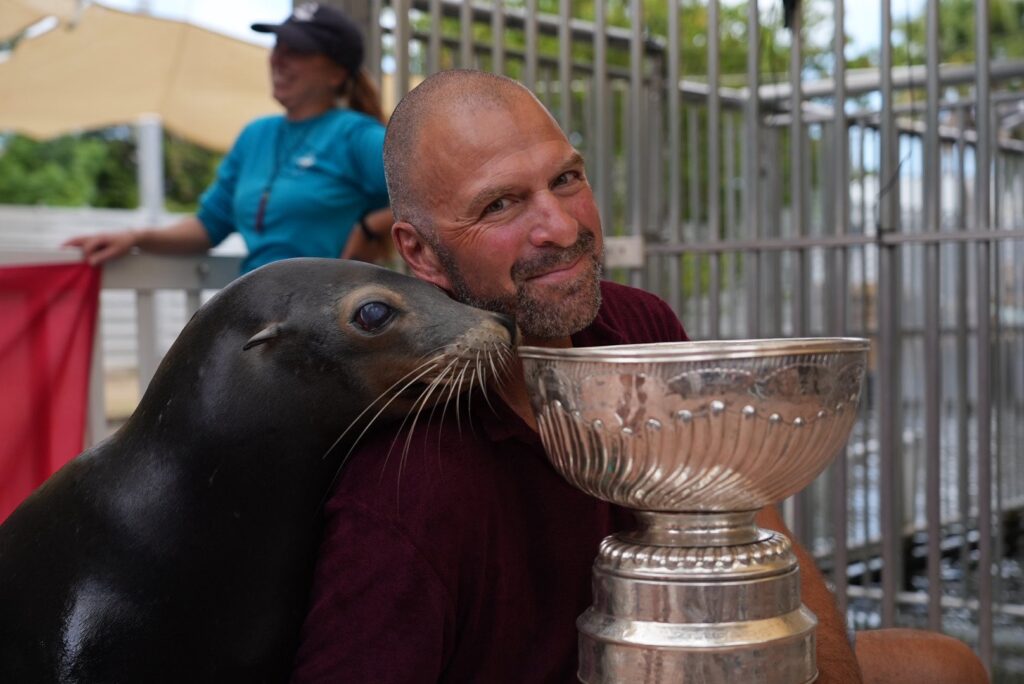 A man holding a trophy with a seal next to him.