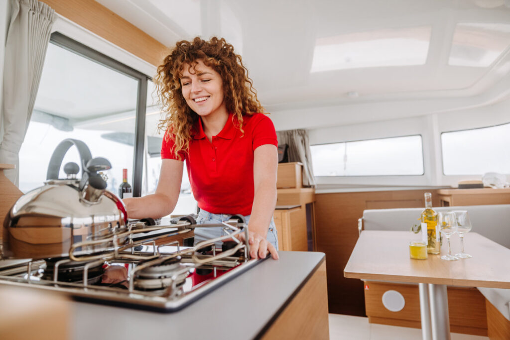 Yacht Detailing | Guide To Services, Costs & Expert Tips | YATCO A smiling woman standing near the stove inside a yacht galley. A smiling woman standing near the stove inside a yacht galley, performing yacht detailing.
