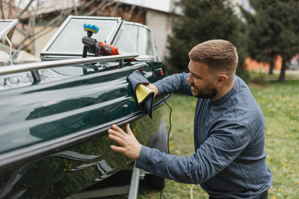 Yacht Detailing | Guide To Services, Costs & Expert Tips | YATCO A person is carefully applying a microfiber cloth to the polished surface of a boat.