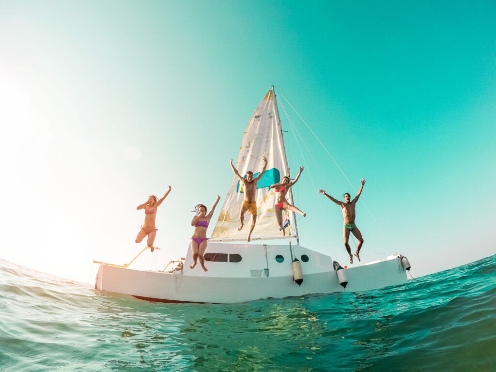 Yacht Party | Guide | Luxury, Locations & What to Wear | YATCO Young people jumping inside ocean in summer vacation.