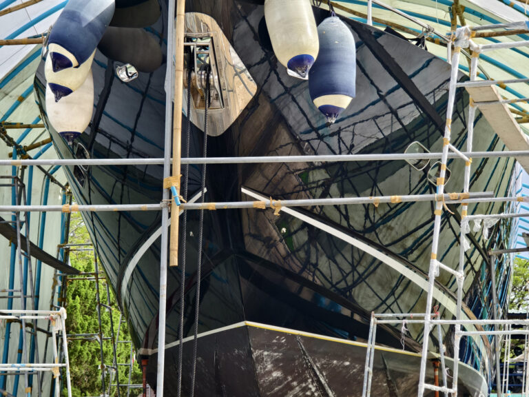 Boat flipping: A boat is carefully lifted under a covered structure for essential maintenance, showcasing preparations and tools. Discover the secrets of boat flipping. Learn how to buy, renovate, and sell boats for profit, from speed boats to project yachts.