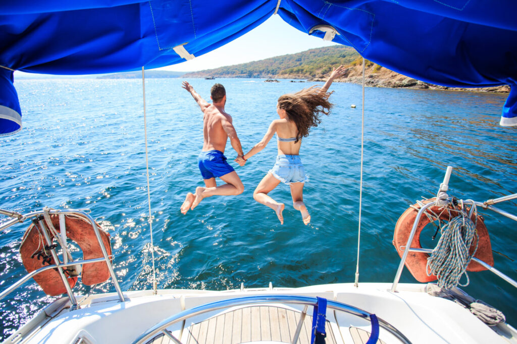 Honeymoon Yacht Charter | Romantic Routes | YATCO Rear view of couple holding hands and jumping into water from yacht during their honeymoon yacht charter.