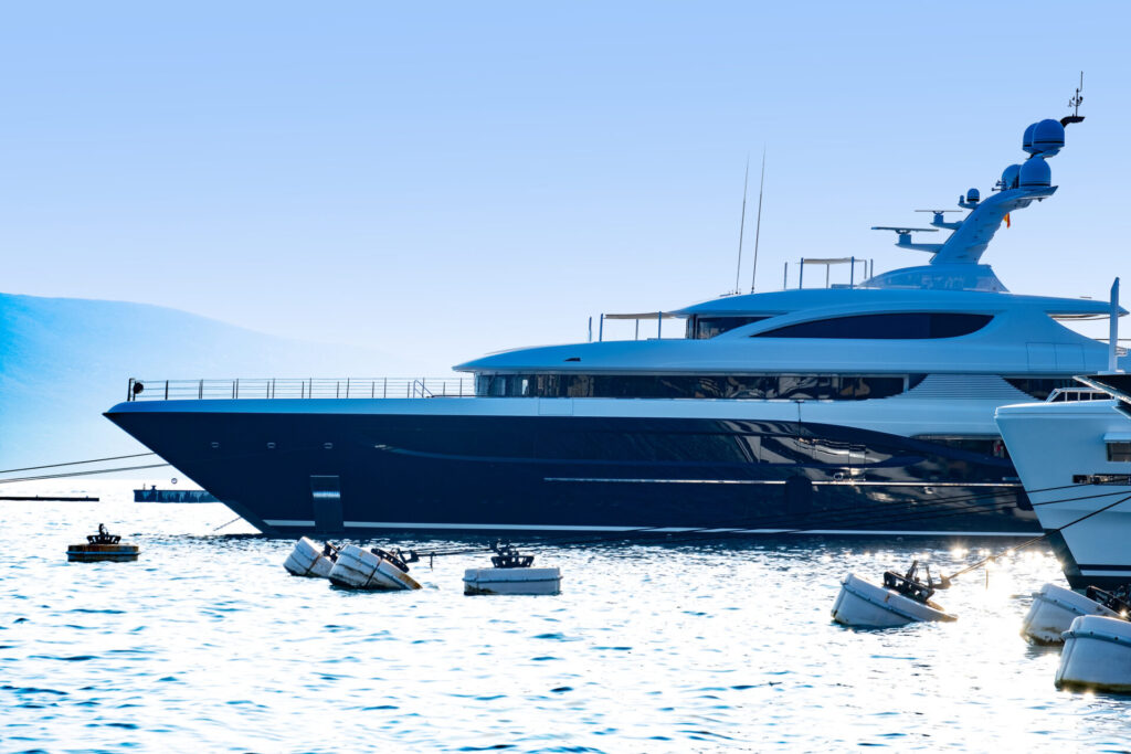 Luxury Yacht Charter Cost vs Budget | What to Expect | YATCO Sleek luxury yachts lined up in coastal Modern Upscale marina, backed by port Montenegro, contemporary Tivat resort and towering green mountains. Uncover how luxury yacht charter costs compare to budget options, from prices and services to Caribbean and Mediterranean destinations.