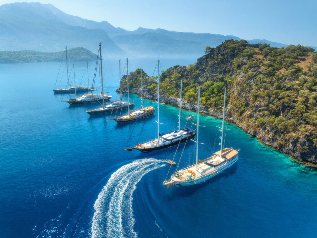 Luxury Yacht Charter Cost vs Budget | What to Expect | YATCO Aerial view of beautiful yachts and boats on the sea at sunset in summer. Uncover how luxury yacht charter costs compare to budget options, from prices and services to Caribbean and Mediterranean destinations.