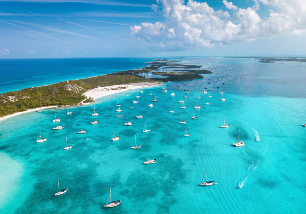 Short Term Yacht Rental | High-End Experiences | YATCO Aerial view of the numerous moored sailboats and yachts at the coast of Stocking Island, The Exumas, Bahamas.