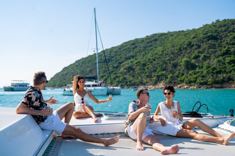 Group of Caucasian man and woman friends enjoy party drinking champagne with talking together while catamaran boat sailing at summer sunset on a short term yacht rental. Short term yacht rental is booming. Learn what’s behind this trend, what to expect, and how it compares to long-term luxury yacht charters.