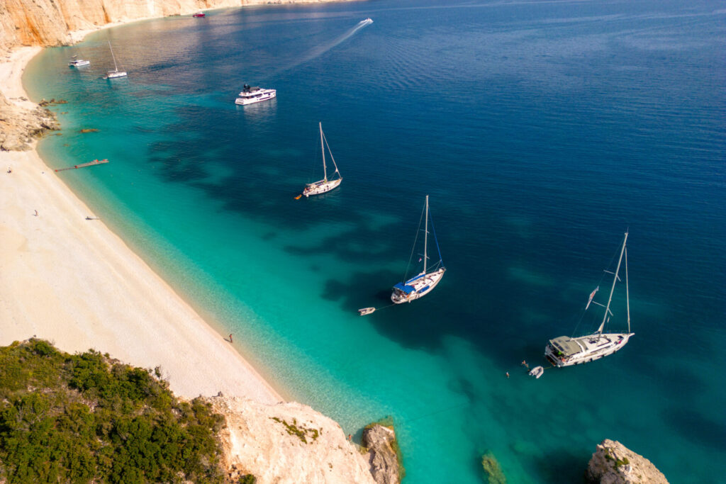 Beautiful lagoon of Fteri beach on Kefalobia, Greece. There are six sailboats anchored in the lagoon, and the sea is crystal clear, blue and turquoise.