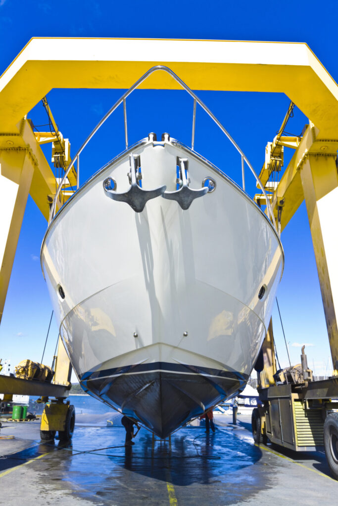 Large luxury used yacht hanging from a shipyard crane and being washed with a high pressure water cleaner. Discover how to inspect used yachts with our expert checklist. Learn what to look for when buying a used boat in 2025.