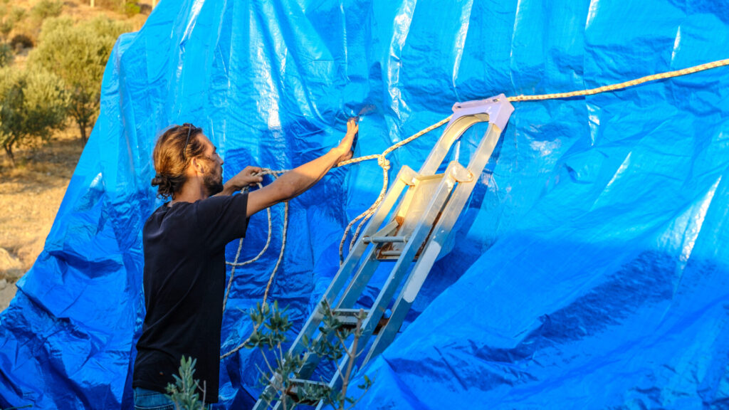 Winterizing a Boat | Guide for Owners | YATCO A man tying his boat, covered with a blue tarp, with ropes while it's on land, winterizing a boat.