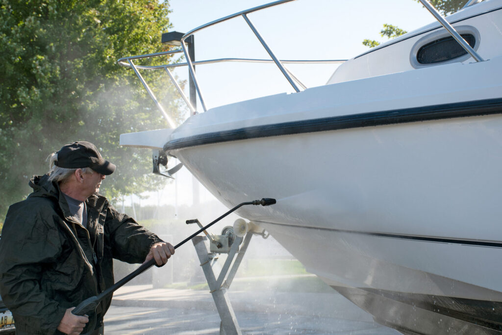 Winterizing a Boat | Guide for Owners | YATCO Caucasian man using pressure washer to clean boat hull while winterizing the boat.