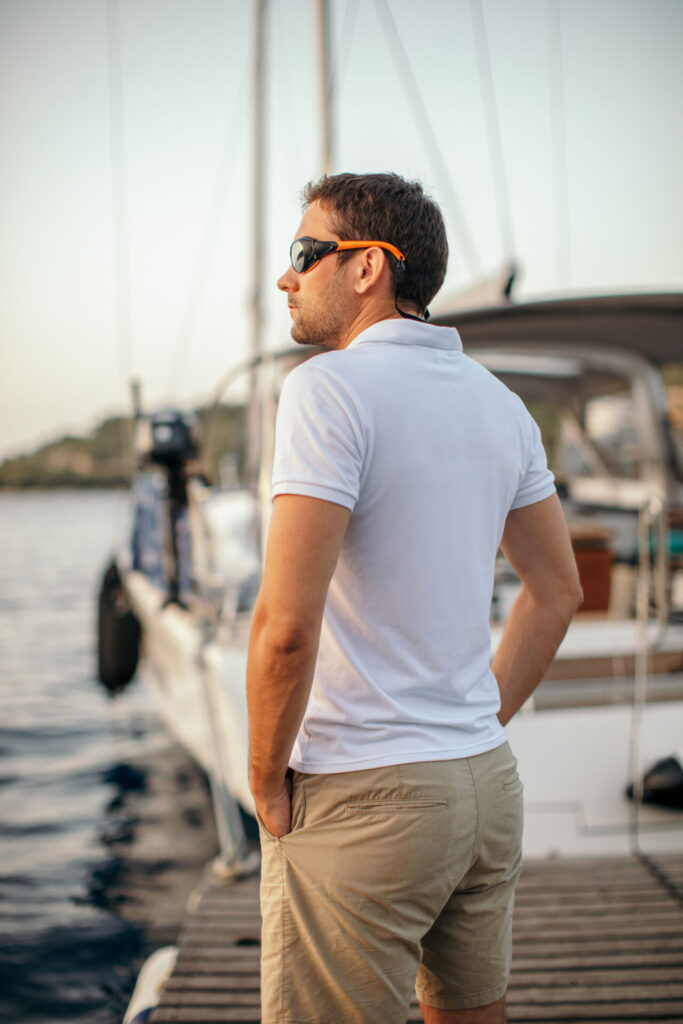 Handsome mid adult skipper on sailboat walking on pier next to his yacht and looking at distance.