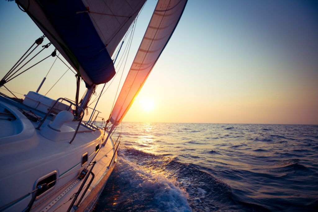Sail boat gliding in open sea at sunset. Explore the best luxury yachts for world circumnavigation for sailing around the globe safely, efficiently, and comfortably.