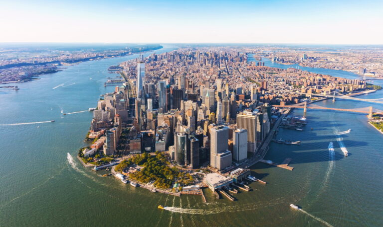 A breathtaking aerial view of Lower Manhattan, surrounded by the Hudson and East Rivers, with its dense skyline and busy waterways filled with boats.