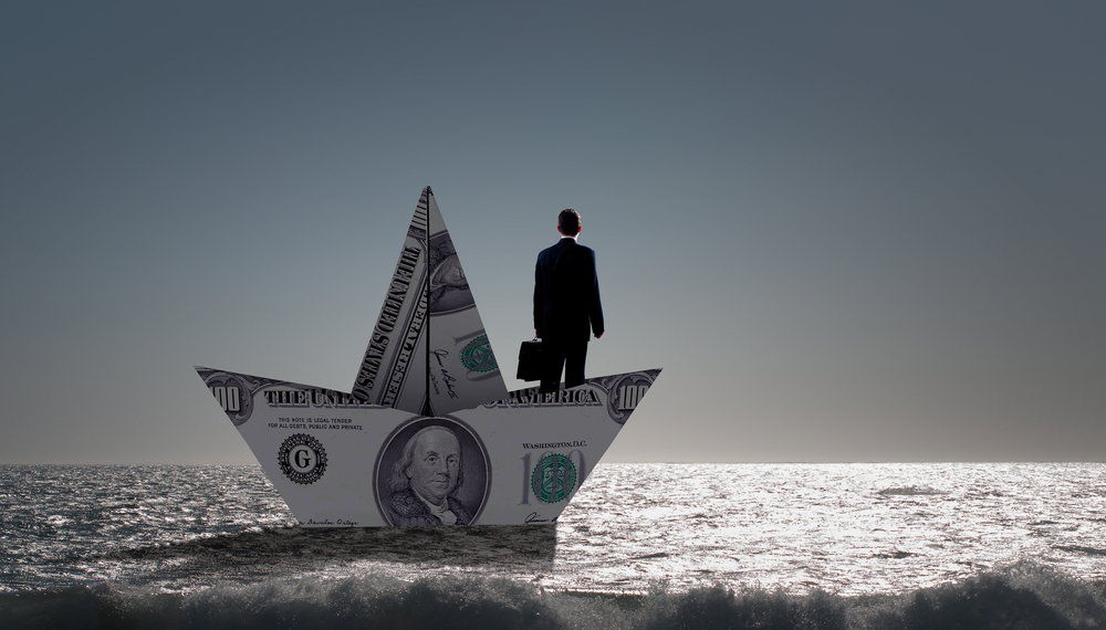 New Economics of yacht ownership. A man standing on a boat made from dollars.